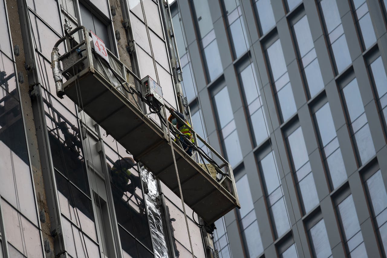 Workers on a suspended platform cleaning windows of a high-rise building in a cityscape.